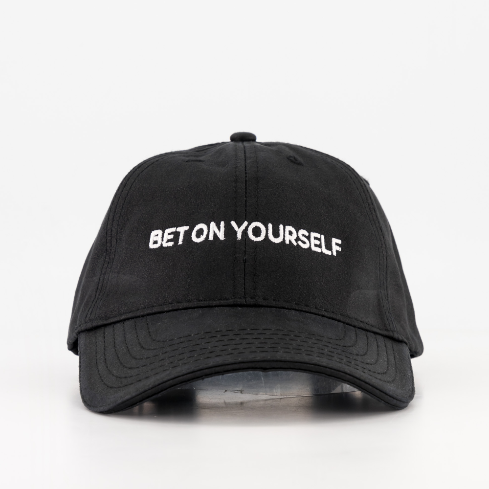 A black baseball cap with the phrase 'BET ON YOURSELF' written in white letters on the front. From the brand BIGTYNSONLY.